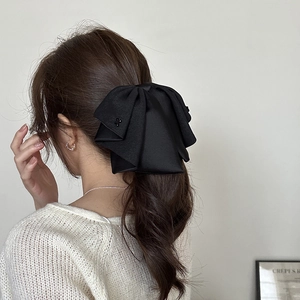 Detail view of a large black satin bow hair clip with beaded floral accents on a model