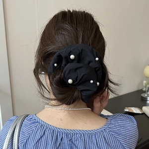 Détail d'un chouchou en tissu noir orné de perles d'imitation porté dans les cheveux