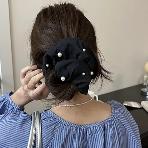 Gros plan d'un chouchou noir oversize avec perles sur un chignon décontracté