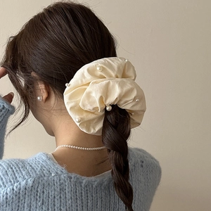 Détail d'un chouchou en tissu crème orné de perles blanches sur une chevelure tressée