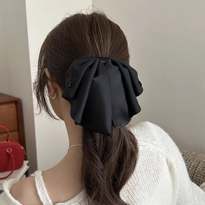 Detail of a black satin bow hair clip with 3D flower accents on a low ponytail