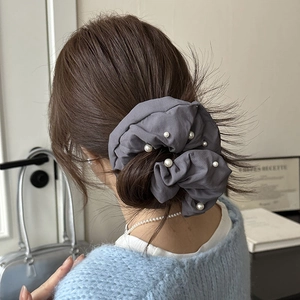 Détail d'un chouchou en tissu plissé gris avec perles blanches sur une coiffure en queue