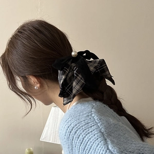 Detail view of plaid bow hair scrunchie with large white pearl on model's hairstyle