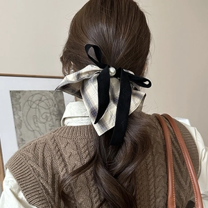 Detail of a brown plaid bow scrunchie with a velvet ribbon and large pearl on wavy hair