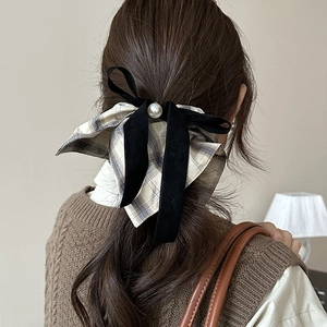 Detail of a large plaid bow hair scrunchie with a velvet ribbon and a white pearl on a model