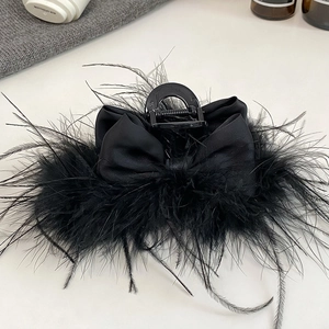 Detail view of a black satin bow hair claw clip with fluffy ostrich feathers on a grey knit surface