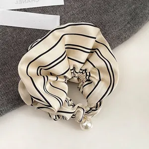 Detailed macro view of champagne striped silk scrunchie with elegant pearl charm detail