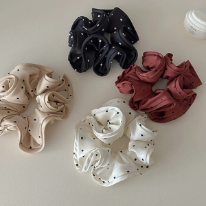 Detailed view of four satin polka dot scrunchies in black, pink, red, and cream silk fabric