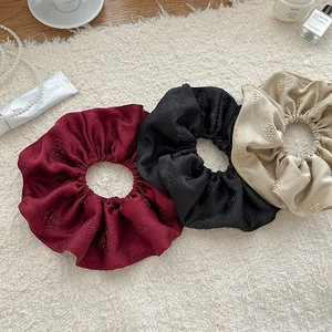 Detail of three jacquard satin scrunchies with camellia relief on white plush