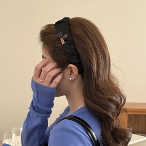 Detail view of black pleated fabric headband with button accent and Hand Made label