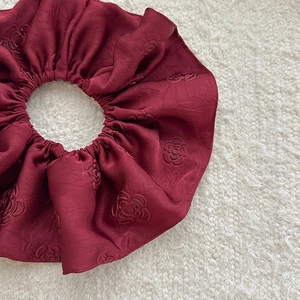 Macro shot of burgundy jacquard satin scrunchie with embossed camellia floral pattern