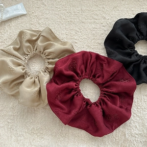 Detail of three jacquard satin scrunchies with rose embossing in champagne and red
