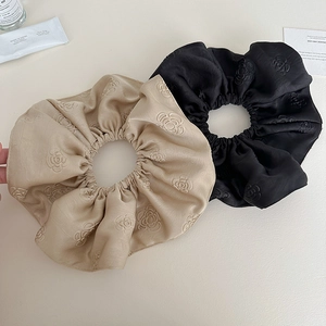 Close-up of champagne and black satin scrunchies featuring 3D camellia floral texture