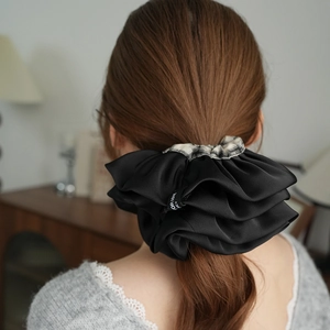 Dettaglio di scrunchie in raso nero con bordo a scacchi su acconciatura a coda di cavallo bassa