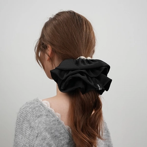 Dettaglio di un elastico per capelli scrunchie in raso nero su una coda di cavallo