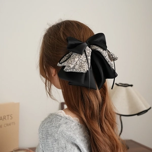 Detail view of a large layered floral and black satin bow hair clip on a model