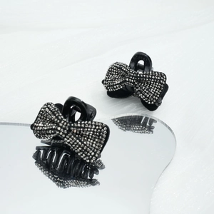 Pince à cheveux noeud noir de 4,5 cm avec strass présentée sur une surface miroir