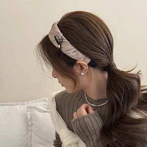 Detail of satin pleated headband in champagne with small black bow detail on model