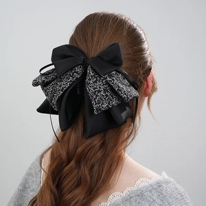 Elegant black layered bow hair clip with white floral pattern on a satin fabric