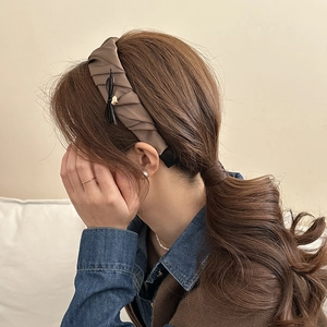 Detail of a brown pleated satin headband with ribbon bow and gold heart charm on a model