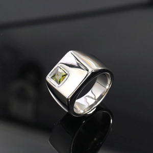 Detalle macro de anillo de sello cuadrado plateado con gema verde sobre espejo