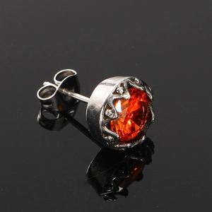 Gros plan d'un clou d'oreille en acier titane argenté avec un zircon orange rond