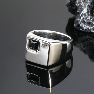 Primer plano macro de un anillo de sello plateado con acabado pulido y una piedra negra cuadrada