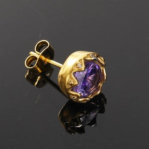 Gros plan d'une puce d'oreille dorée vintage avec une grande pierre violette et diamants