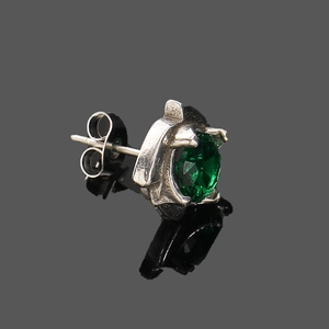 Gros plan d'une boucle d'oreille vintage en argent avec un zircon vert éclatant