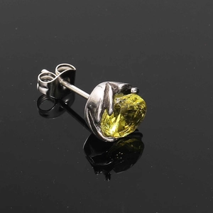 Macro shot of silver claw-set stud earring featuring a brilliant round yellow stone