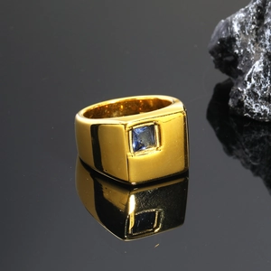 Primer plano de un anillo dorado pulido con gema azul cuadrada en fondo negro elegante