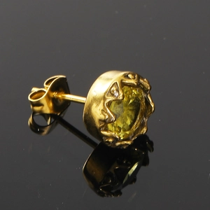 Détail d'un clou d'oreille en titane doré avec pierre vert-jaune sertie couronne sur miroir