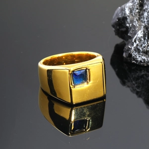 Primer plano de un anillo dorado de hombre con zafiro azul sobre fondo oscuro espejo
