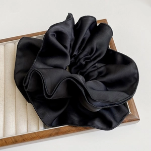 Elegant large black satin scrunchie with soft ruffled texture on a velvet tray