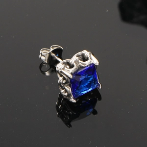 Dettaglio macro di orecchino con zircone blu e trama vintage a rilievo su acciaio