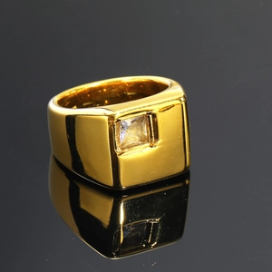 Primer plano de un anillo de titanio dorado con circonita cuadrada sobre fondo brillante