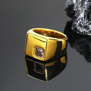 Primer plano de anillo de sello dorado con gema rosa cuadrada sobre piedra oscura