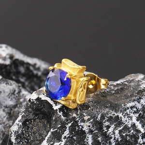 Macro shot of a square blue zircon earring with a vintage golden engraved setting on dark rock