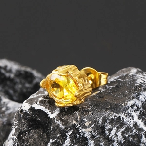 Close-up of golden lava texture stud earring with yellow oval zircon on volcanic rock