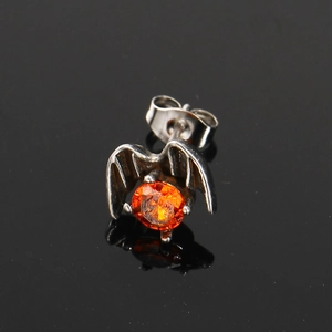 Macro shot of gothic bat wing stud earring with orange zircon stone on black surface