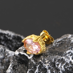 Detail of pink oval-cut zircon stud earring in gold finish on black stone background