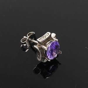 Macro view of silver titanium steel stud earring with oval purple zircon and vintage relief