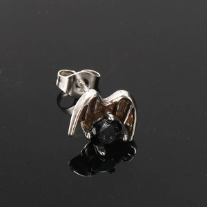 Macro shot of punk gothic wing earring with black zircon stone on mirrored base