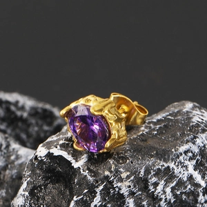 Macro shot of gold-plated stud earring with purple zircon on natural black rock background