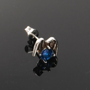 Macro shot of punk style wing-shaped earring with blue zircon on black reflective surface