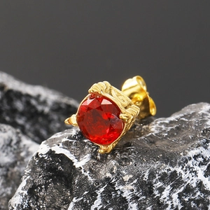 Vista macro del pendiente chapado en oro con circón rojo sobre fondo de piedra oscura
