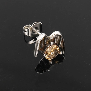 Detail of punk silver wing stud earring with amber zircon on a black reflective surface