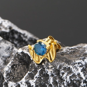 Macro view of a gold bat wing stud earring featuring a faceted round blue zircon stone