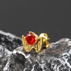 Macro shot of gold punk wing claw earring with red zircon on dark volcanic rock