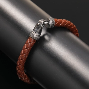 Detailed close-up of brown braided leather bracelet with vintage engraved metal clasp